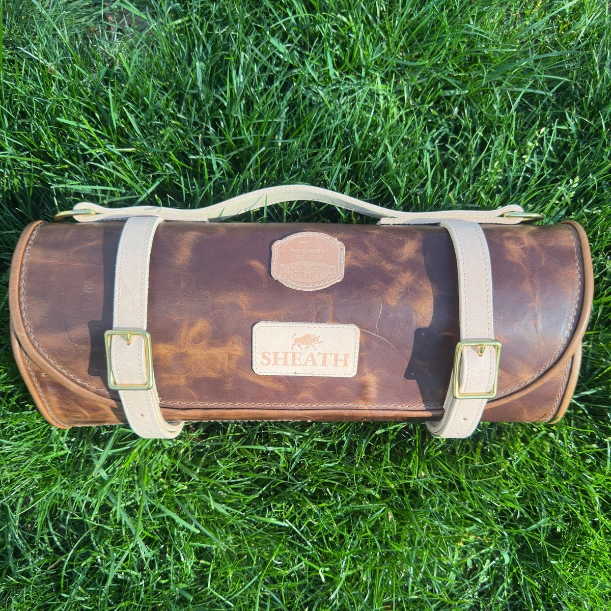 Brown leather knife roll with visible branding on grass
