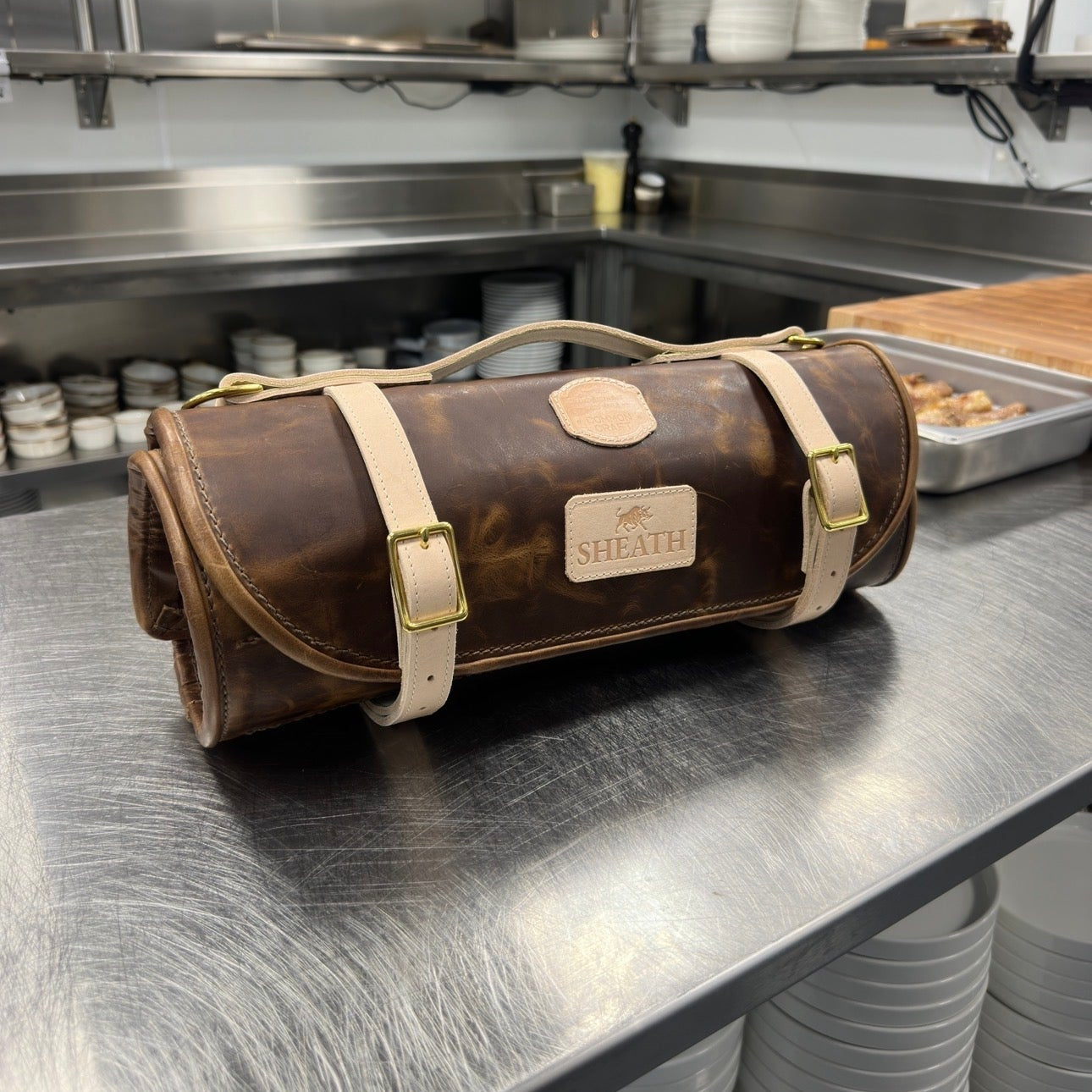 Brown knife roll with beige straps on a metal surface in a kitchen setting